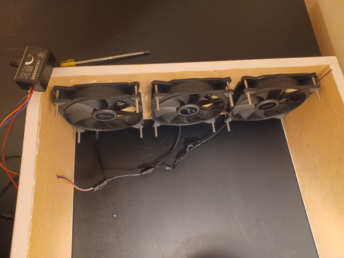 Three black computer fans are screwed into the inside of a wooden frame. A knob rests atop the frame, and a screwdriver sits just past it.