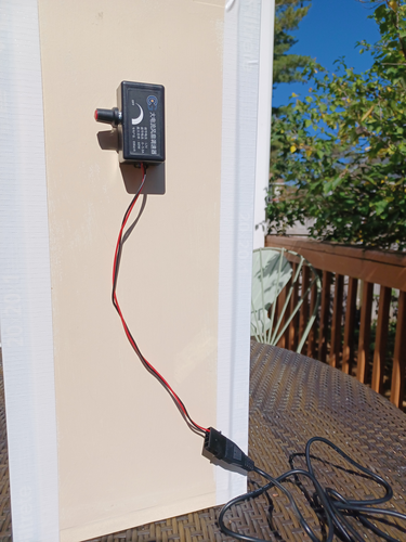 Two wires hang from a knob assembly on a wooden frame atop a wicker table. A plug hanging from the wires attaches to a sturdier cable.